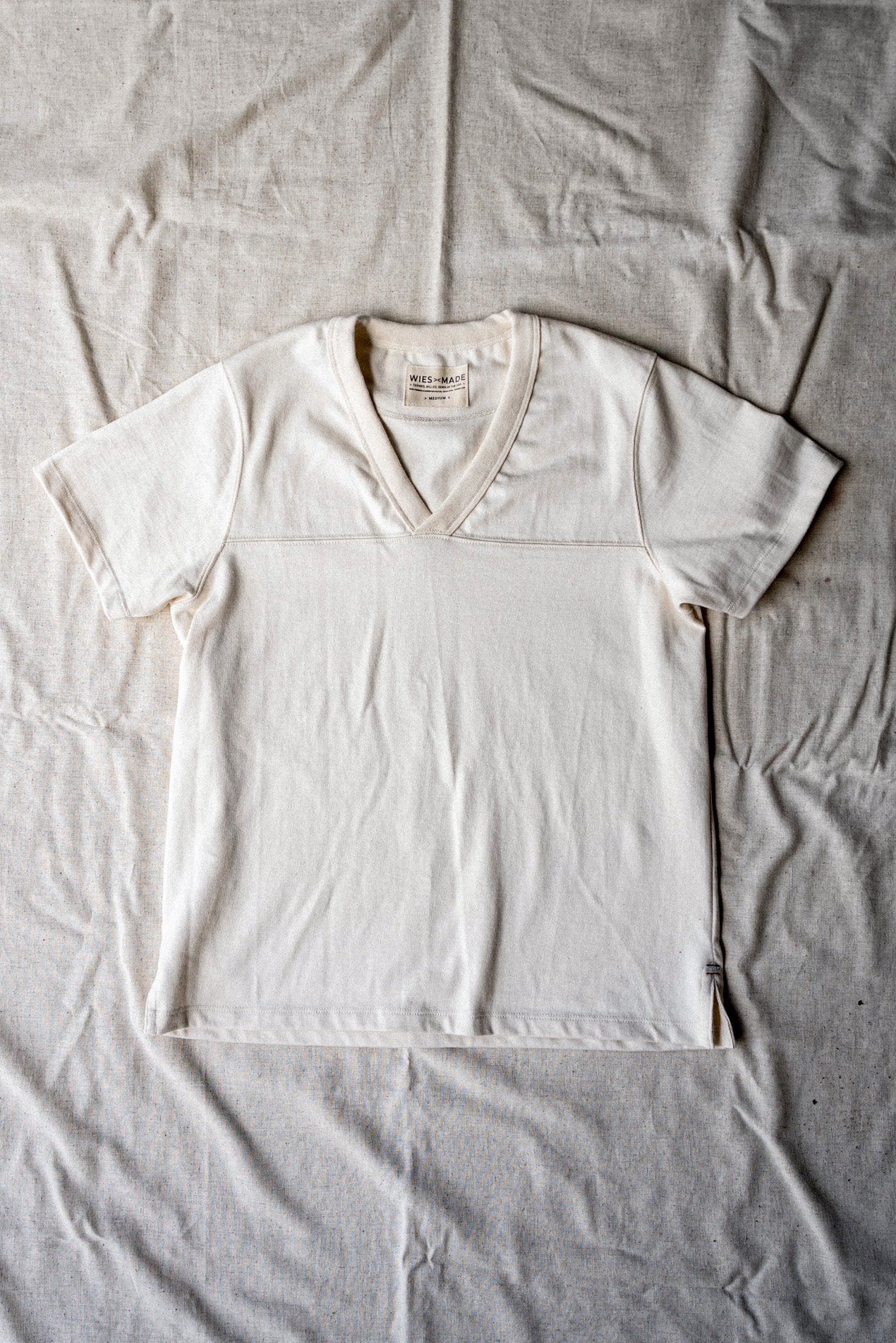 Natural cotton women's V-neck jersey tee laid flat, showing yoke seam and WiesMade label.