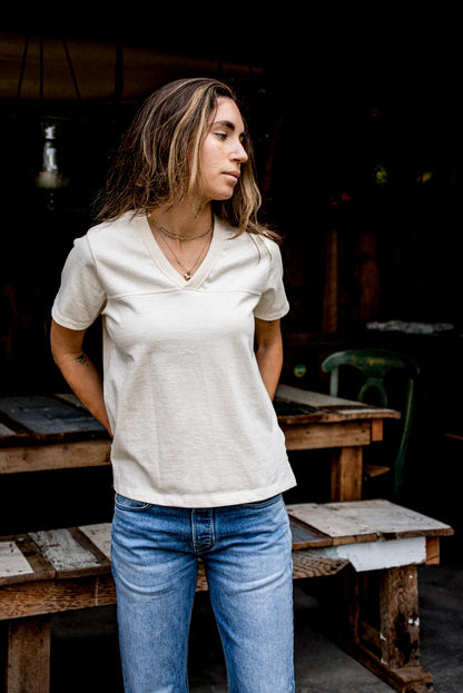 Model wearing natural cotton Stinson V-neck jersey tee with jeans by rustic wood benches.
