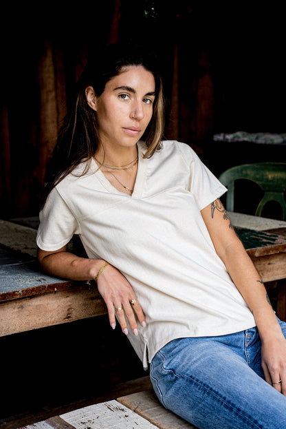 Model wears the natural Stinson V-neck cotton jersey with jeans, seated on rustic wood.