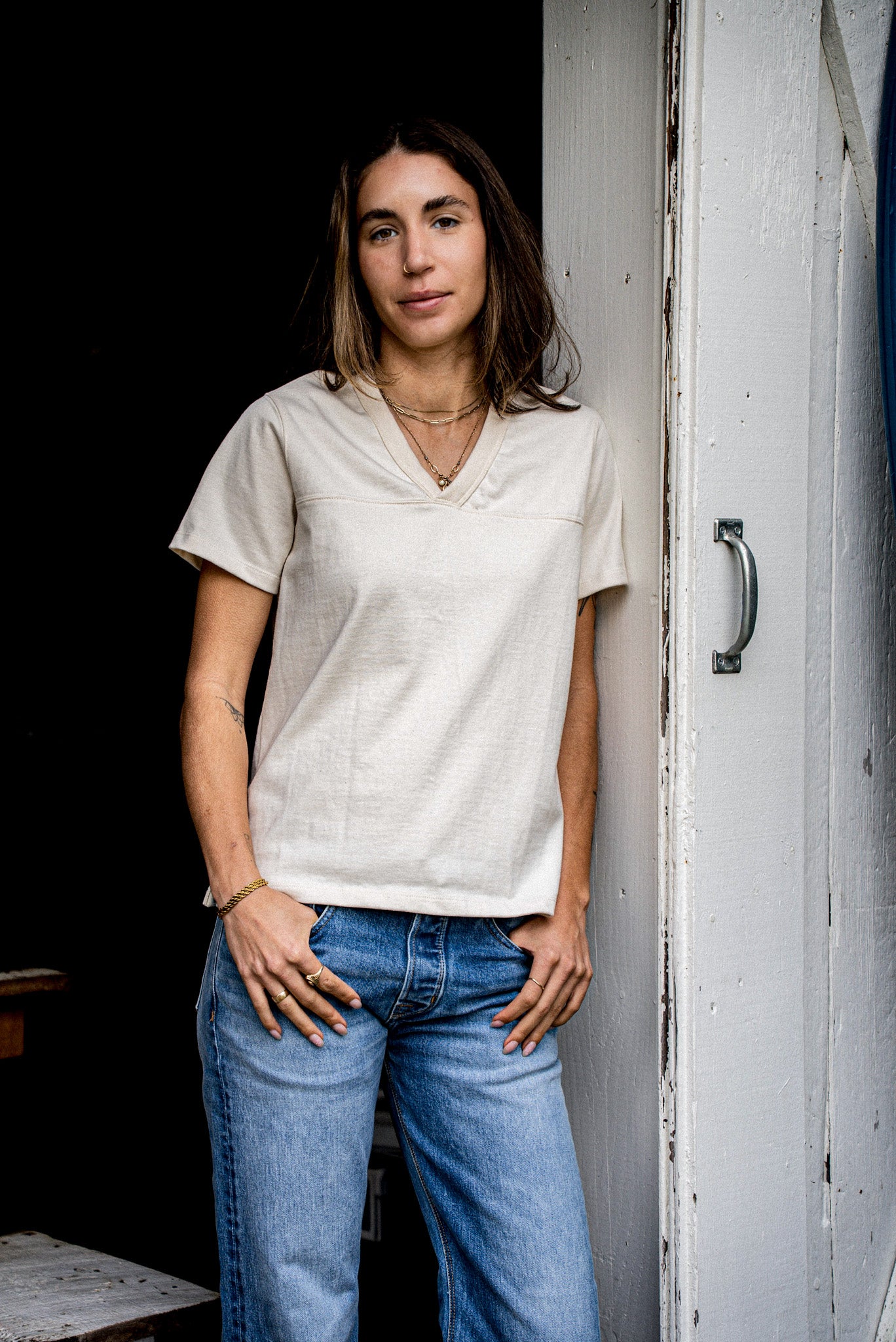 Person in natural 12oz cotton Stinson V-neck jersey top, styled with blue jeans by a doorway.