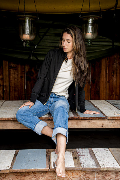 Open black cotton moto jacket with brass zipper worn over a cream tee and jeans.