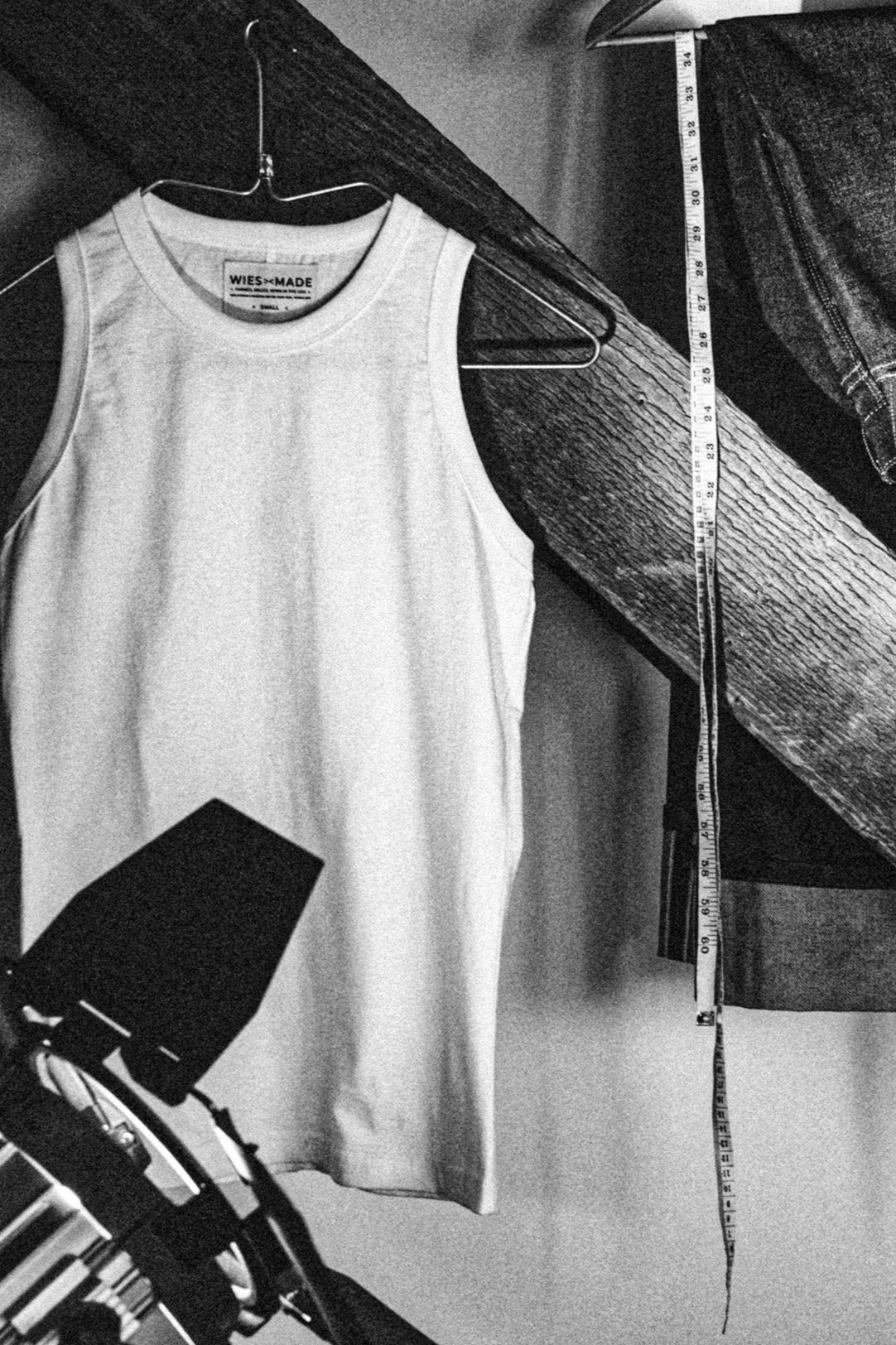 Reyes boxy tank in polar white on a hanger beside selvedge denim and a tailor's measuring tape.