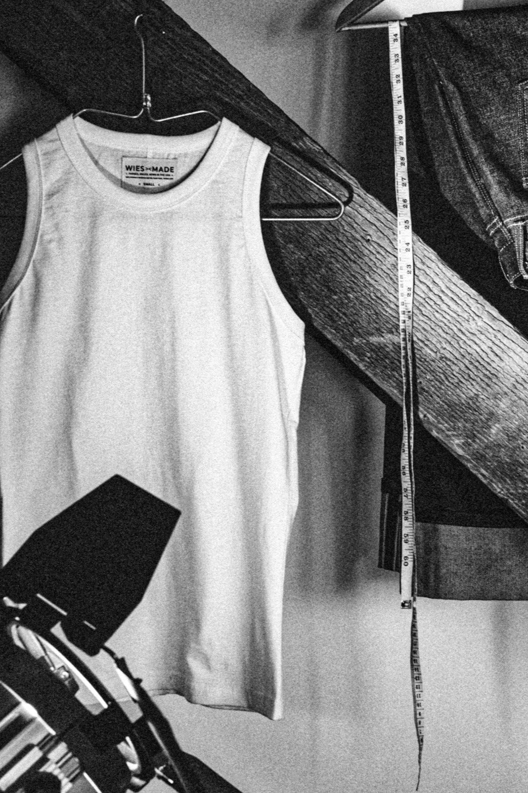 Reyes boxy cotton tank top on a hanger beside a measuring tape and folded selvedge denim in a workshop.