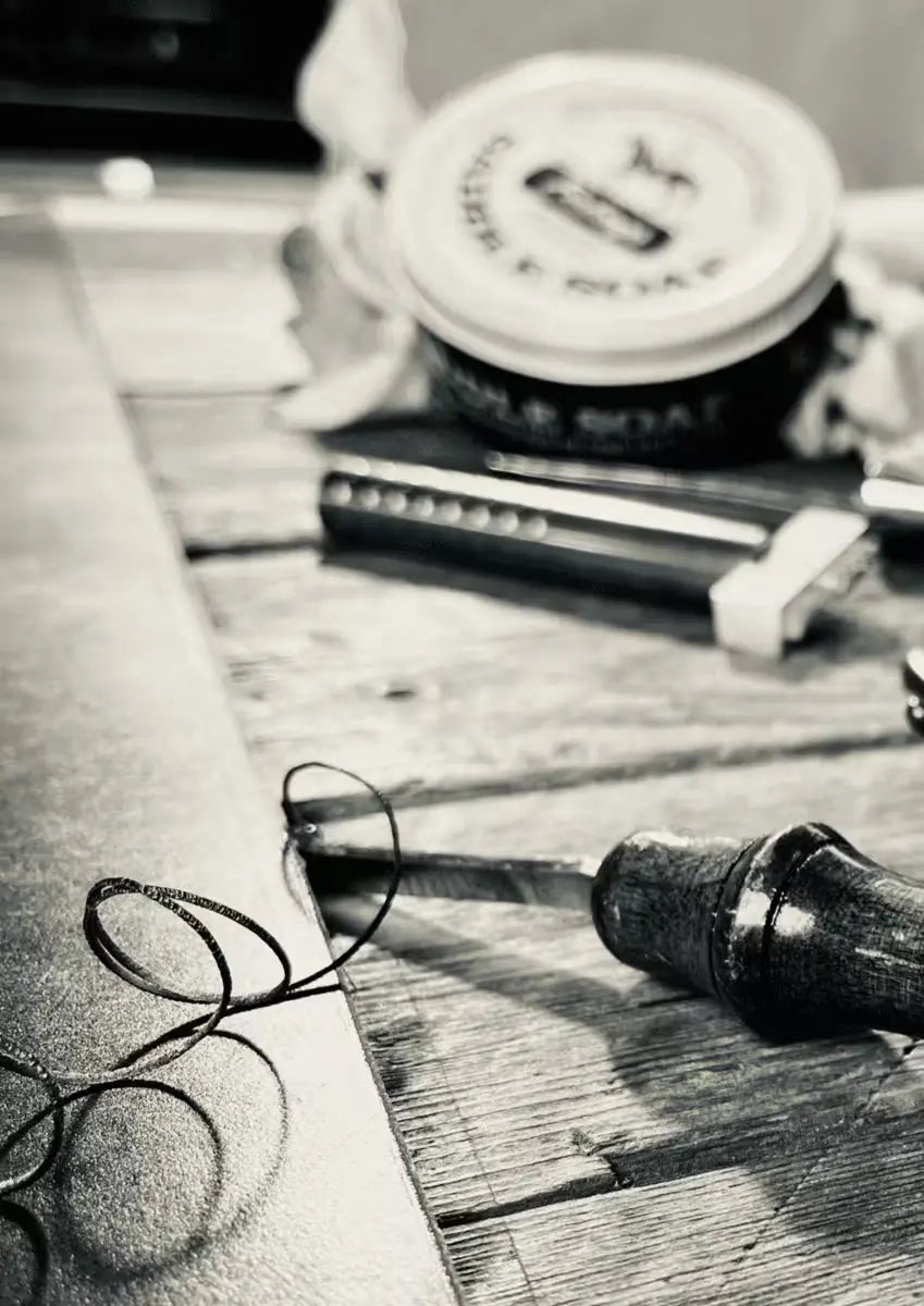 Leatherworking tools and black thread on a wooden surface, showcasing craftsmanship for creating an 8oz Latigo Belt in black and white filter