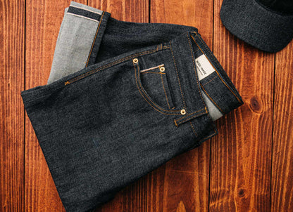 Selvedge denim jeans made in the USA neatly folded on a wooden surface, showcasing premium raw denim texture, reinforced stitching, and traditional craftsmanship for timeless quality