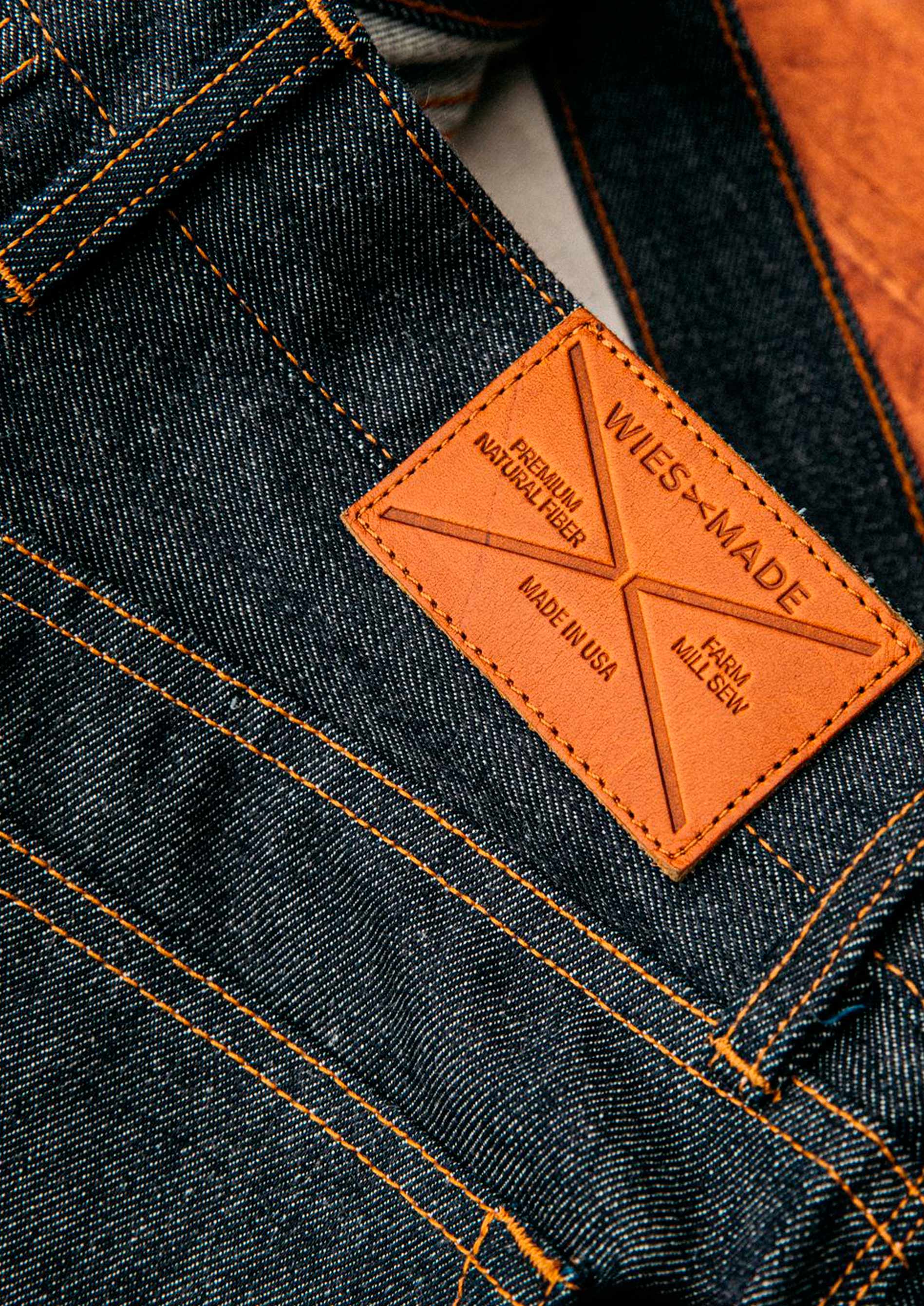 American made selvedge denim close-up featuring rich indigo weave, copper stitching, and a WiesMade tan leather patch