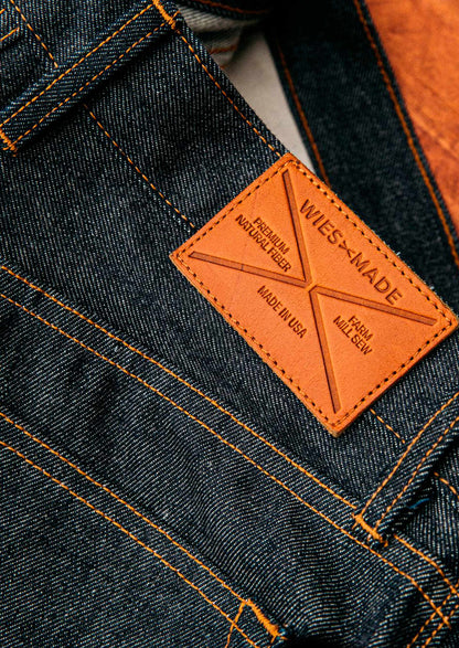 American made selvedge denim close-up featuring rich indigo weave, copper stitching, and a WiesMade tan leather patch